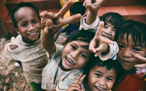 five children smiling while doing peace hand sign