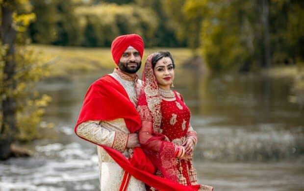 A couple in traditional Indian wedding attire standing on a rock by a river