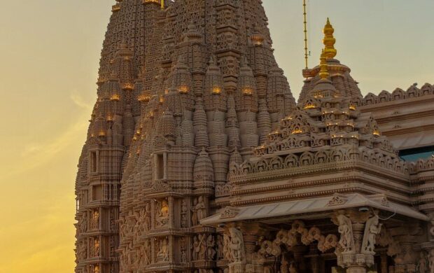 Intricately carved stone temple towers with golden spires against a warm orange sky